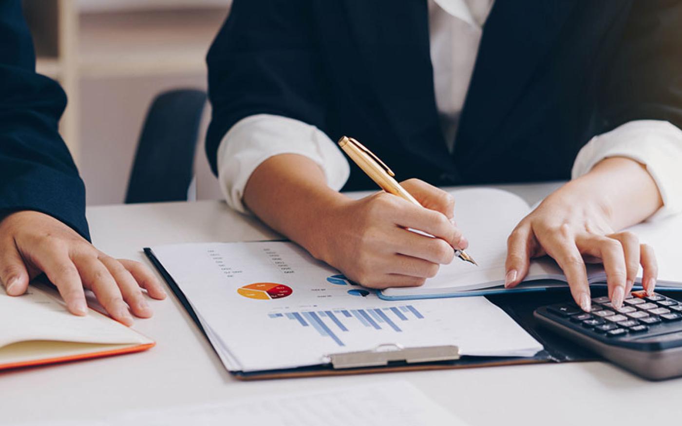 Two people working at a table in an office using a calculator.